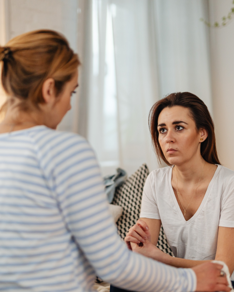 Zwei Frauen sitzen sich gegenüber – eine hört still und aufmerksam zu, während die andere spricht.