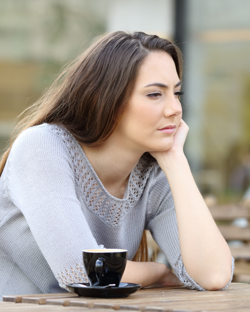 Frau sitzt nachdenklich an einem Tisch mit Kaffee – ein Moment des Innehaltens und Reflektierens.